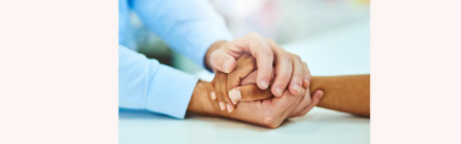 A person's hand holding the hand of another person on a beige background